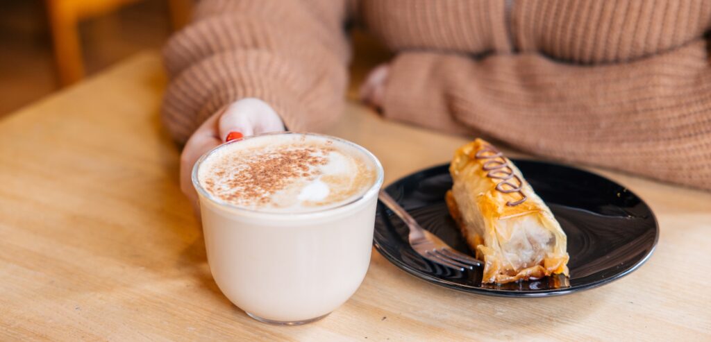 A person holds a latte topped with classic latte art, accompanied by a small plate of baklava at Wolf Hills Coffee.
