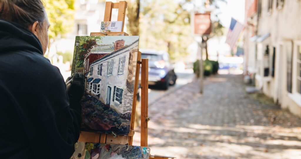 An artist paints an outdoor scene of The Tavern during the Plein Air Abingdon festival, capturing the historic building and surrounding streetscape on canvas.