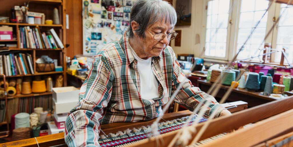 Resident artist Nancy Garretson works at her loom inside The Arts Depot, surrounded by her weaving materials and artwork.